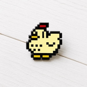 Könnte beinhalten: Ein Pixel-Art-Emaille-Pin in Form eines hellgelben Huhns mit schwarzer Umrandung. Das Huhn hat einen kleinen roten Kamm auf dem Kopf, einen gelben Schnabel und zwei gelbe Füße. Das Design ist in einem blockartigen, digitalen Stil mit schwarzen Akzenten gehalten.