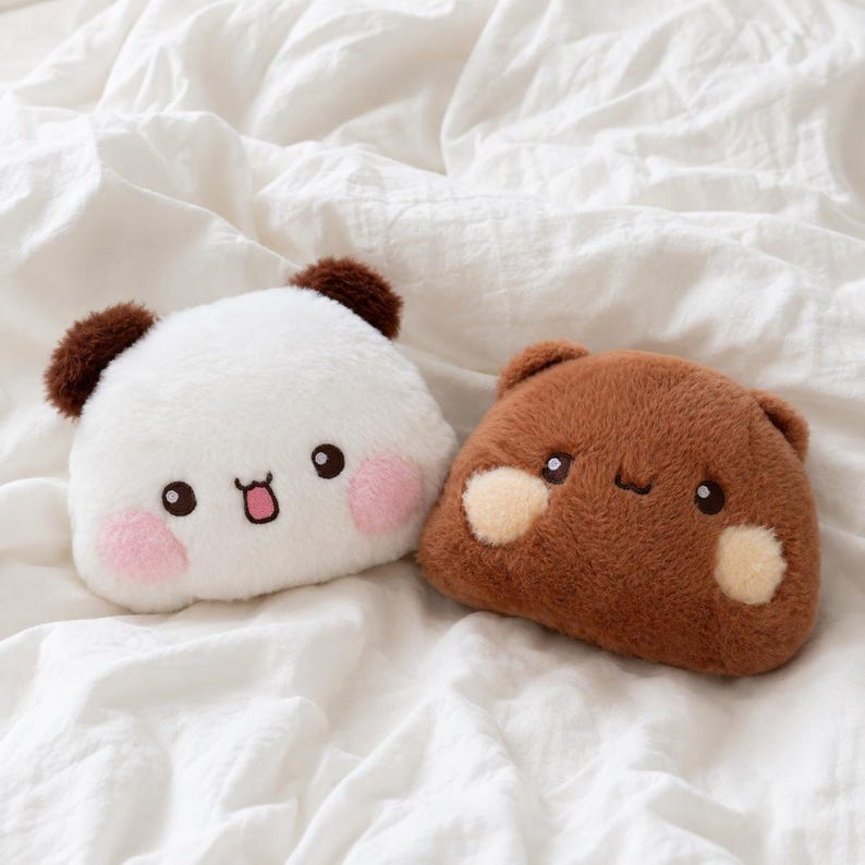 May include: Two plush animal-shaped pillows with soft fur. One is white with dark brown ears, black eyes, a small mouth, and pink cheeks. The other is brown with matching ears, black eyes, a simple mouth, and light beige circular cheek patches.
