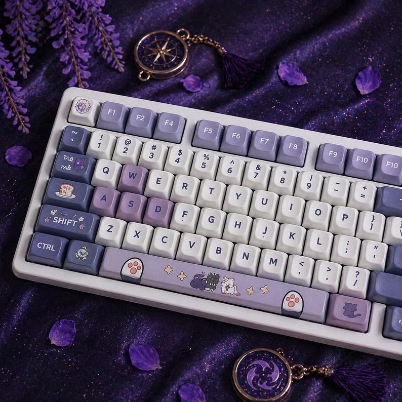 May include: A white and purple mechanical keyboard with custom keycaps. The keycaps feature a mix of white, purple, and blue colors. The keyboard has a cat paw design on the spacebar and other cat-themed keycaps. A compass pendant and purple flowers are in the background.