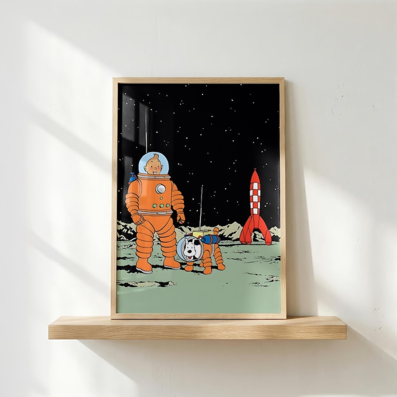 May include: A framed art print featuring a cartoon character in an orange space suit and a white dog in a matching space suit standing on a green lunar surface. A red and white checkered rocket stands in the background against a black starry sky.
