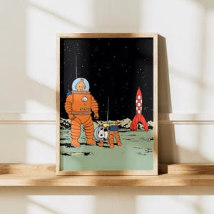 May include: A framed art print featuring a cartoon character in an orange space suit and a white dog in a matching space suit standing on a green lunar surface. A red and white rocket stands in the background against a black starry night sky.