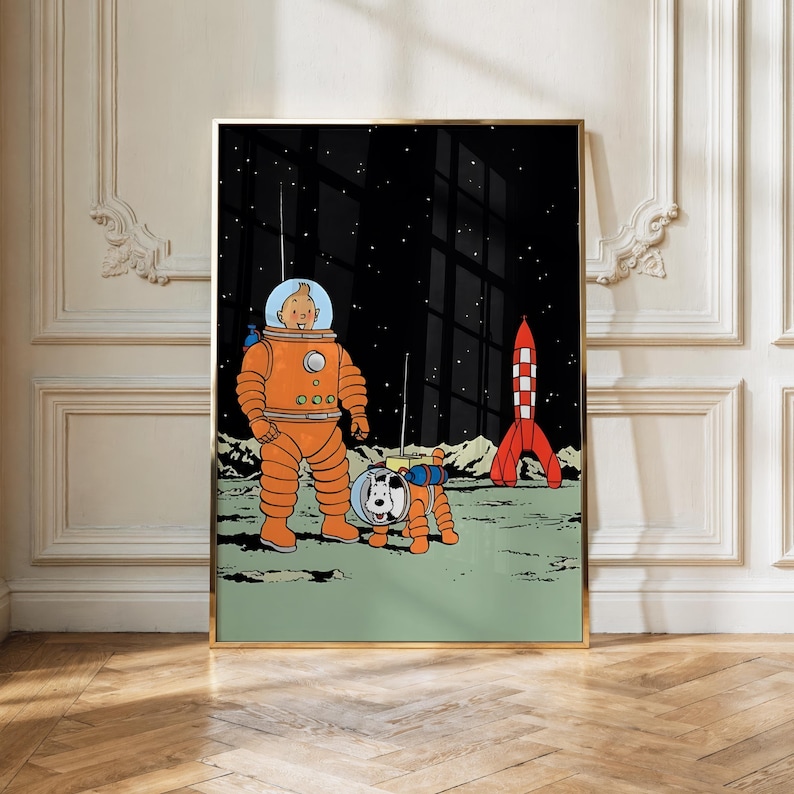 May include: A framed wall art print featuring a comic illustration of a character in an orange spacesuit and a white dog in a matching orange spacesuit standing on a green lunar surface with a red and white rocket ship against a black starry sky.