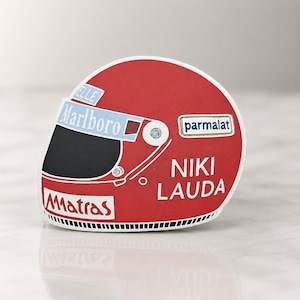 May include: A red and white racing helmet with the text "NIKI LAUDA" in white. The helmet features the "Marlboro" and "Parmalat" logos, and the "Matras" logo. The helmet has a black visor.