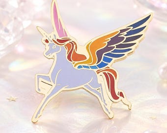 Könnte beinhalten: Ein goldfarbener Einhorn-Anstecker mit hellblauem Körper, bunten Flügeln und einer rosa-roten Mähne. Der Anstecker zeigt ein laufendes Einhorn mit Horn und detailliertem Design. Ein dekoratives Accessoire.