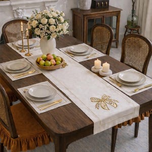 Può includere: Un tavolo da pranzo apparecchiato per un pasto, con un tavolo in legno scuro, un runner e dei sottopiatti bianchi. Il tavolo è apparecchiato con piatti, posate dorate e candele. Un centrotavola di rose bianche e una ciotola di mele completano l'arredamento.