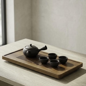 May include: A black ceramic tea set on a wooden tray. The set includes a teapot with a curved spout and three small teacups. The tray has a rectangular shape with a slatted design.