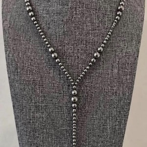 Puede incluir: Un collar en forma de Y que presenta una serie de cuentas metálicas pulidas en tono plateado. Las cuentas varían en tamaño, con esferas más grandes situadas en la parte superior y central, que pasan a cuentas más pequeñas a lo largo de la cadena.