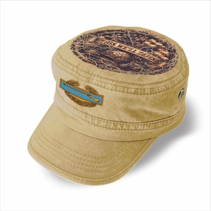 May include: A tan military-style cadet cap featuring a circular graphic on the top with the text THIS WE'LL DEFEND and a central infantry badge emblem on the front panel, displaying a light blue rifle icon surrounded by a gold-coloured wreath.