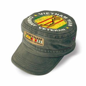 May include: An olive green military-style cap featuring a rectangular patch on the front that reads VIETNAM COMBAT VETERAN with a ribbon graphic. The top of the cap displays a circular graphic of the map of Vietnam with the text VIETNAM WAR COMBAT VETERAN.
