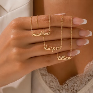 May include: Three gold-toned metal necklaces, each featuring a delicate chain and a nameplate pendant. The pendants display the names madison, harper, and lillian in a cursive script font. The necklaces are displayed together, showcasing the thin links.