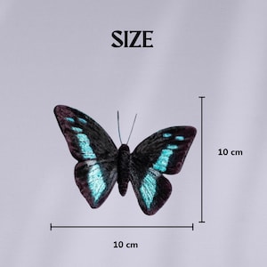 May include: A black and teal butterfly with a 10 cm wingspan is displayed against a light gray background. The word "SIZE" is printed above the butterfly. The butterfly's wings have teal accents.
