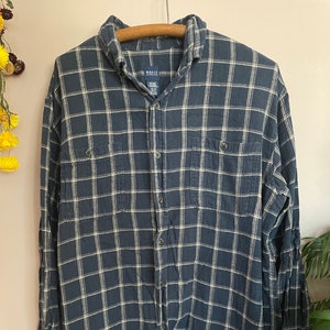 May include: A blue and white plaid long-sleeve button-down shirt with two chest pockets. The shirt has a Basic Editions label.