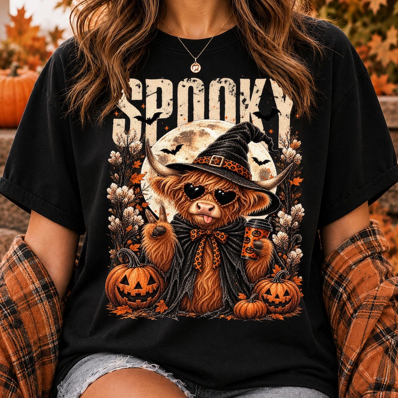May include: A black t-shirt featuring a graphic of a fluffy highland cow wearing a witch hat, heart-shaped sunglasses, and a cape. The cow holds a coffee cup and makes a peace sign. The text SPOOKY appears above, with pumpkins and a moon.