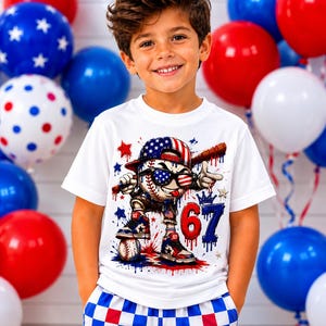 May include: A white short-sleeve t-shirt featuring a graphic of a baseball character wearing a flag-patterned cap and sunglasses, holding a bat. The design includes the number 67 in red and blue, with red and blue paint splatter accents.