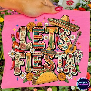 May include: Pink t-shirt with the words "LET'S FIESTA" in a colorful, decorative font. The design includes a sombrero, guitar, taco, chili peppers, and a sugar skull, evoking a festive Mexican theme.