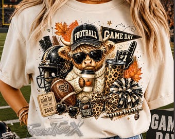 May include: A beige t-shirt featuring a graphic of a Highland cow wearing a football cap and sunglasses, holding a coffee cup. The design includes a football helmet, a leopard print tumbler, a football, a ticket labeled ADMIT ONE 2026, and a bow.