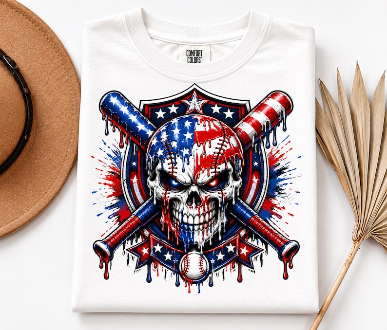 May include: A white t-shirt with a Comfort Colors label featuring a graphic of a skull painted like an American flag, positioned in front of two crossed baseball bats. The design includes red, white, and blue paint drips, stars, and a baseball.