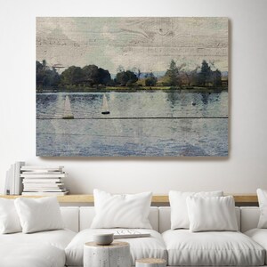 May include: A painting of a lake with sailboats on the water. The lake is surrounded by trees and the sky is a light blue. The painting is on a wooden background.
