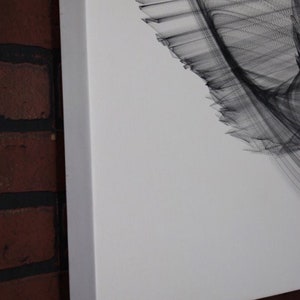 May include: A close-up of a white canvas with a black abstract design. The design is made up of thin lines that create a swirling pattern.