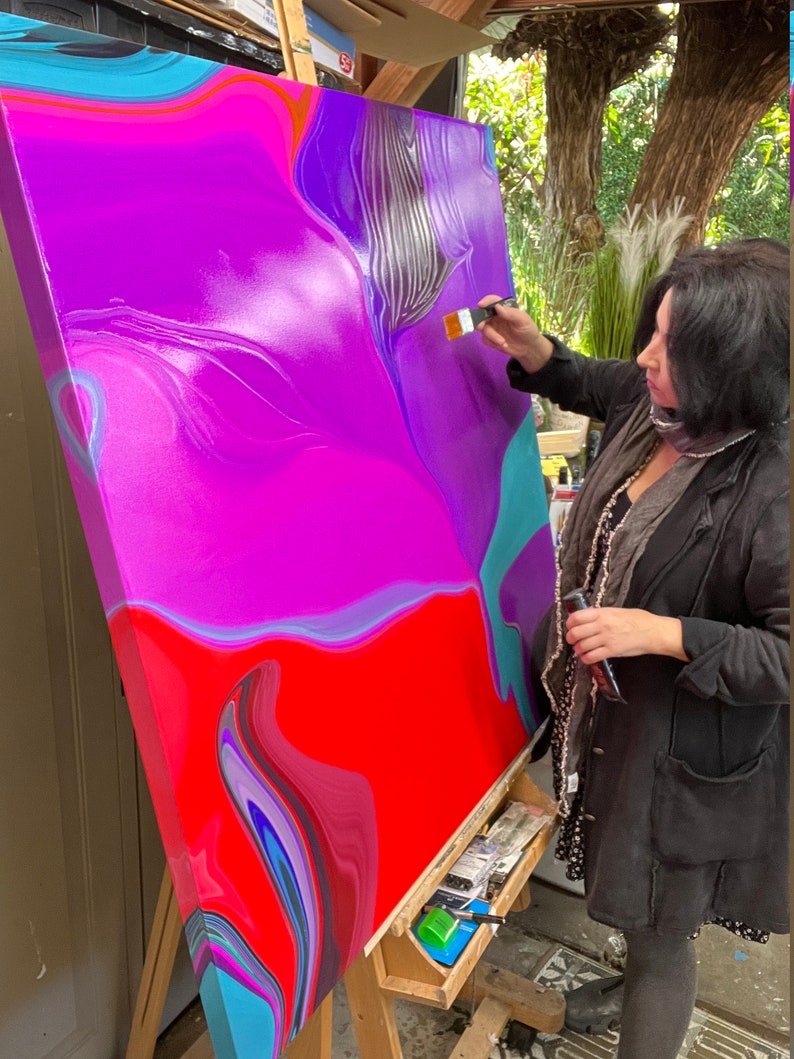 May include: An artist painting a large abstract canvas. The artwork features vibrant colors, including red, purple, and teal, with a fluid, marbled effect. The artist is using a brush to add details to the painting.
