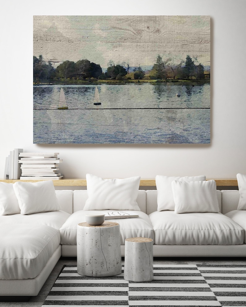 May include: A painting of a lake with sailboats on the water. The lake is surrounded by trees and the sky is a light blue. The painting is on a wooden background.