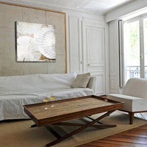 May include: A white couch with a white throw blanket and two glasses of wine on a wooden coffee table with a tray. The couch is in a living room with white walls and a large window with white curtains.
