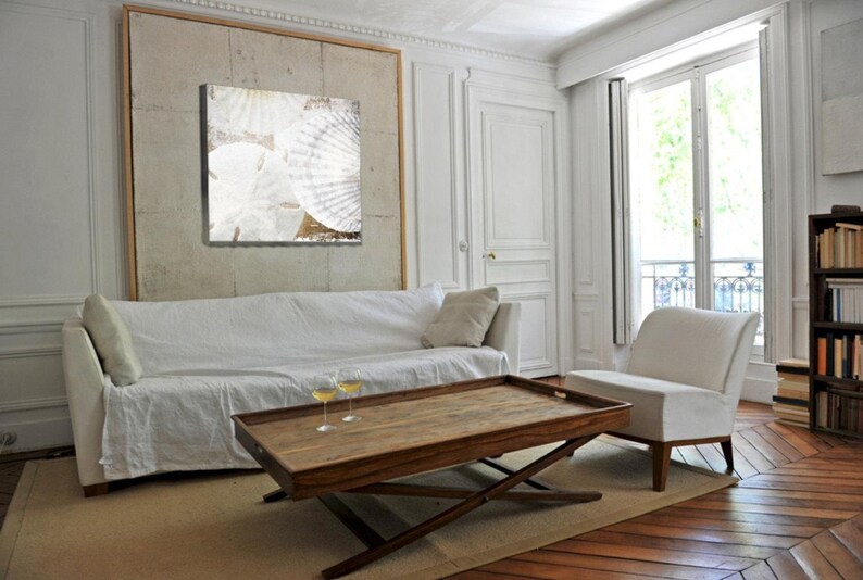 May include: A white couch with a white throw blanket and two glasses of wine on a wooden coffee table with a tray. The couch is in a living room with white walls and a large window with white curtains.