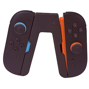 May include: Black and orange game controller with blue and orange accents. The controller has buttons, directional pads, and joysticks. The design is ergonomic and appears to be for a handheld gaming device.