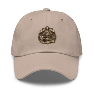 May include: A beige baseball cap featuring a detailed graphic print of the exposure triangle. The design includes an eye within a triangle, camera icons, and text reading "THINK ISO," "THINK APERTURE," "SHUTTER SPEED," and "THE EXPOSURE TRIANGLE."