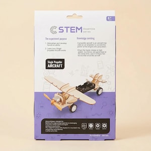 Peut inclure: Un kit STEM Assemble series avec un mod&egrave;le d'avion &agrave; h&eacute;lice unique en bois. La bo&icirc;te est violette et blanche, avec du texte d&eacute;crivant le but de l'exp&eacute;rience et la combinaison des connaissances. Le mod&egrave;le a une h&eacute;lice, des ailes et des roues.
