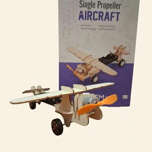 Peut inclure: Maquette d'avion &agrave; h&eacute;lice unique en bois, avec une h&eacute;lice orange et des roues noires. L'emballage indique "Single Propeller AIRCRAFT" avec les mots "science, technology, engineering, mathematics".