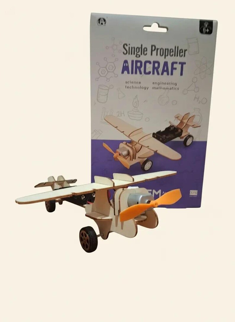Peut inclure: Maquette d'avion &agrave; h&eacute;lice unique en bois, avec une h&eacute;lice orange et des roues noires. L'emballage indique "Single Propeller AIRCRAFT" avec les mots "science, technology, engineering, mathematics".