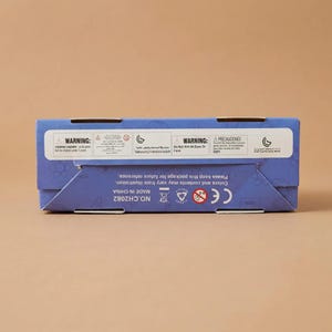 Peut inclure: Une bo&icirc;te en carton bleue avec plusieurs &eacute;tiquettes d'avertissement et du texte. La bo&icirc;te porte une marque CE et le texte "MADE IN CHINA". Le texte "CHOKING HAZARD" est &eacute;galement visible.