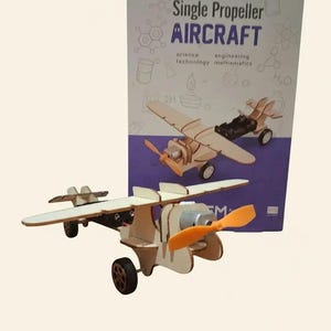 Peut inclure: Maquette d'avion &agrave; h&eacute;lice unique en bois, avec une h&eacute;lice orange et des roues noires. L'emballage indique "Single Propeller AIRCRAFT" avec les mots "science, technology, engineering, mathematics".