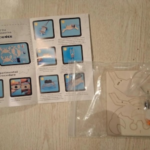 Peut inclure: Un kit scientifique avec un puzzle en bois en forme de crabe et un manuel d'instructions. Le manuel comprend des sch&eacute;mas et du texte, dont "Meet the accessories" et "Experimental procedure". Le puzzle est dans un sac en plastique transparent.
