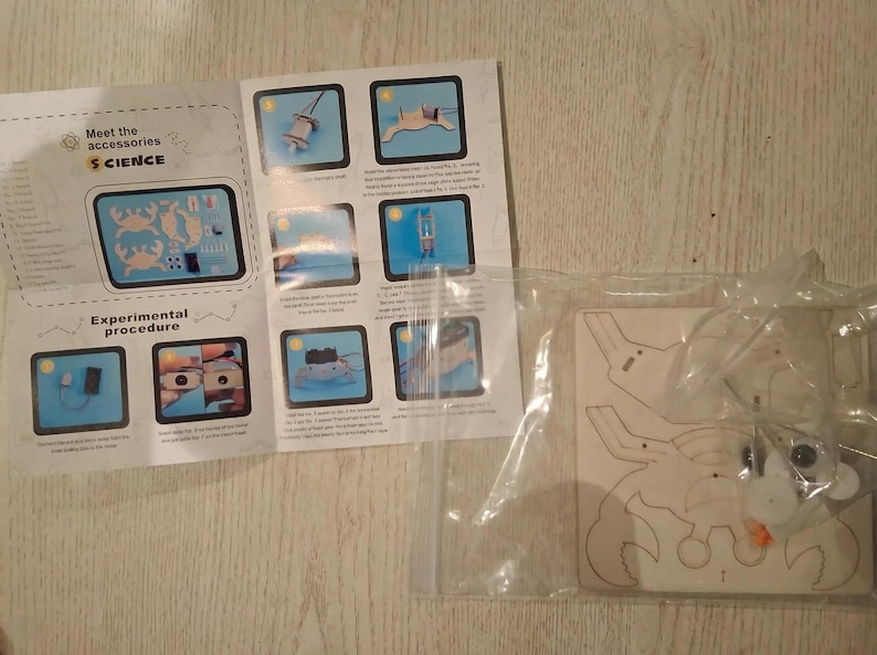 Peut inclure: Un kit scientifique avec un puzzle en bois en forme de crabe et un manuel d'instructions. Le manuel comprend des sch&eacute;mas et du texte, dont "Meet the accessories" et "Experimental procedure". Le puzzle est dans un sac en plastique transparent.