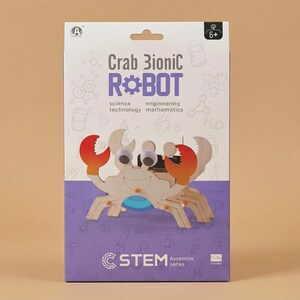 Peut inclure: Un kit de la s&eacute;rie STEM avec un robot bionique crabe en bois. La bo&icirc;te porte l'inscription "Crab Bionic Robot" avec les mots "science, technologie, ing&eacute;nierie, math&eacute;matiques". Le crabe a des pinces rouges et oranges et des yeux globuleux.