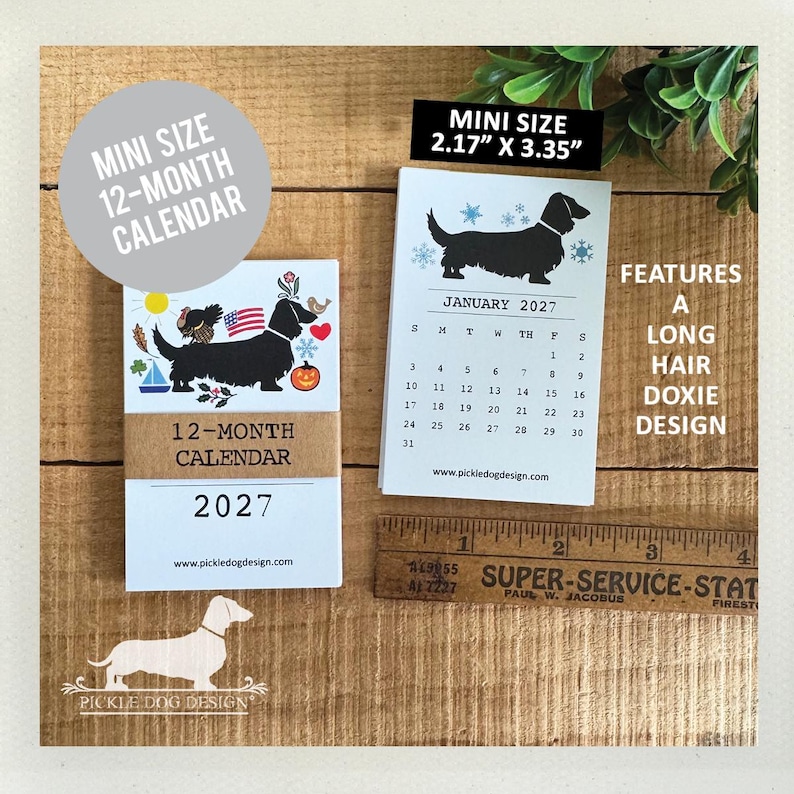 May include: A 2027 mini 12-month calendar featuring a long hair dachshund design. The calendar measures 2.17 inches by 3.35 inches as shown by a wooden ruler. The cover displays a black dog with seasonal icons, and the interior page shows January 2027.