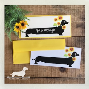 May include: Greeting cards featuring a black dachshund silhouette with sunflowers. The cards have the text "your message" and come with yellow envelopes. The design includes a logo of a dachshund.