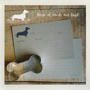 May include: Recipe cards with a dachshund silhouette and the text "Back of cards are lined!" A metal dog bone-shaped cookie cutter is also in the image. The cards have lines for ingredients, directions, and servings.