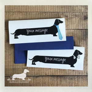 Puede incluir: Tarjetas blancas con ilustraciones de perros salchicha negros con corbata azul y pajarita, con la frase "your message". Se ve un sobre azul. El fondo es de vetas de madera.