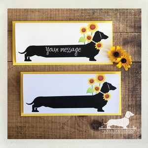 May include: Two greeting cards with a black dachshund silhouette adorned with sunflowers. The cards have a white background with the text "your message" and a yellow border. A few sunflowers are placed on the right side of the cards.