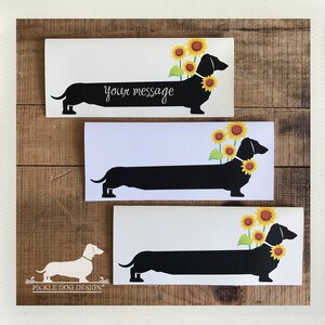 May include: Three white rectangular cards with a black dachshund silhouette wearing a sunflower collar. The top card has the text "your message" in cursive. The cards are on a wooden background.