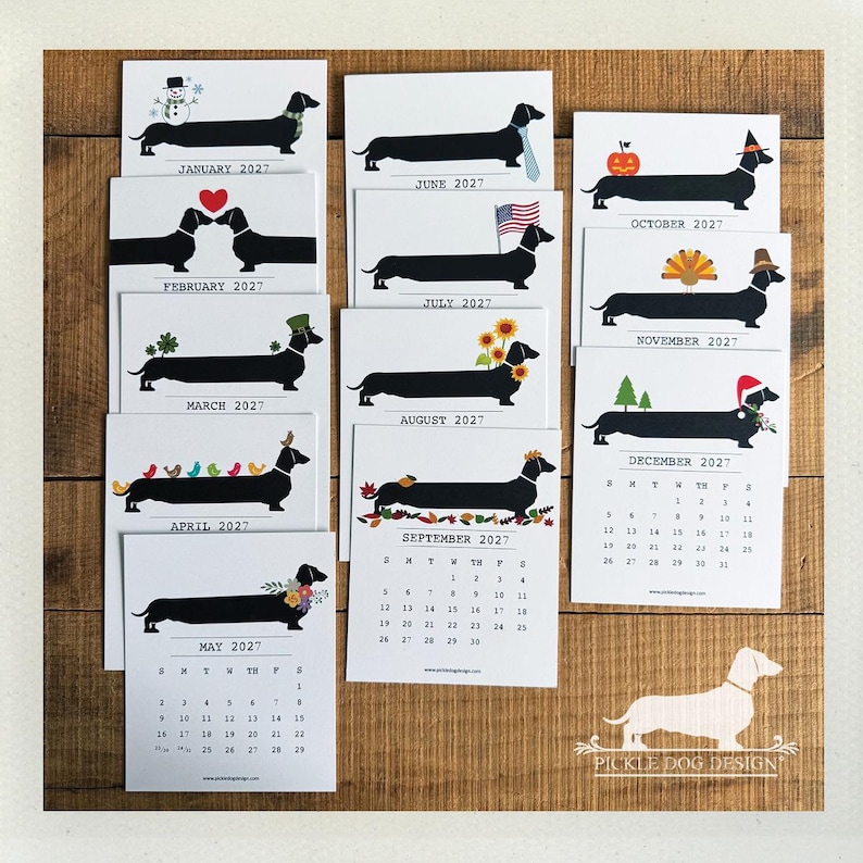 May include: A 2027 wall calendar set featuring twelve individual white cards, each displaying a black silhouette of a dachshund with seasonal illustrations for every month, including holiday themes, flowers, and a calendar grid.