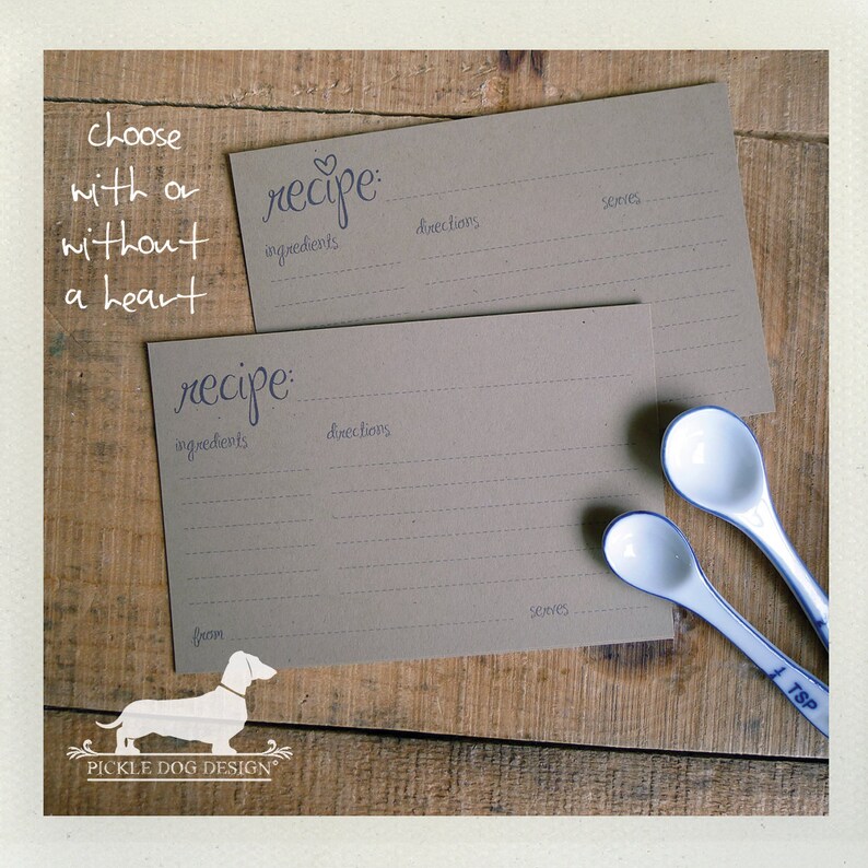 May include: Two recipe cards with the word "recipe" in cursive, with lines for ingredients, directions, and servings. The cards are on a wooden surface with two white and blue measuring spoons. Text reads "choose with or without a heart."