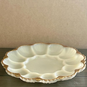 May include: Cream-colored, oval-shaped serving dish with a scalloped edge and gold trim. The dish has multiple compartments, ideal for serving appetizers or snacks. A decorative piece for entertaining.