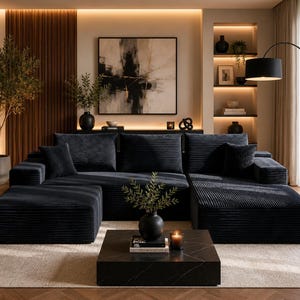 Może przedstawiać: Duża narożna sofa z ciemnoszarego sztruksu z pasującą pufą i dwiema kwadratowymi poduszkami. Sofa posiada teksturowane, prążkowane wykończenie tkaniny oraz niski profil, umieszczona w przestrzeni mieszkalnej z kwadratowym czarnym stolikiem kawowym.