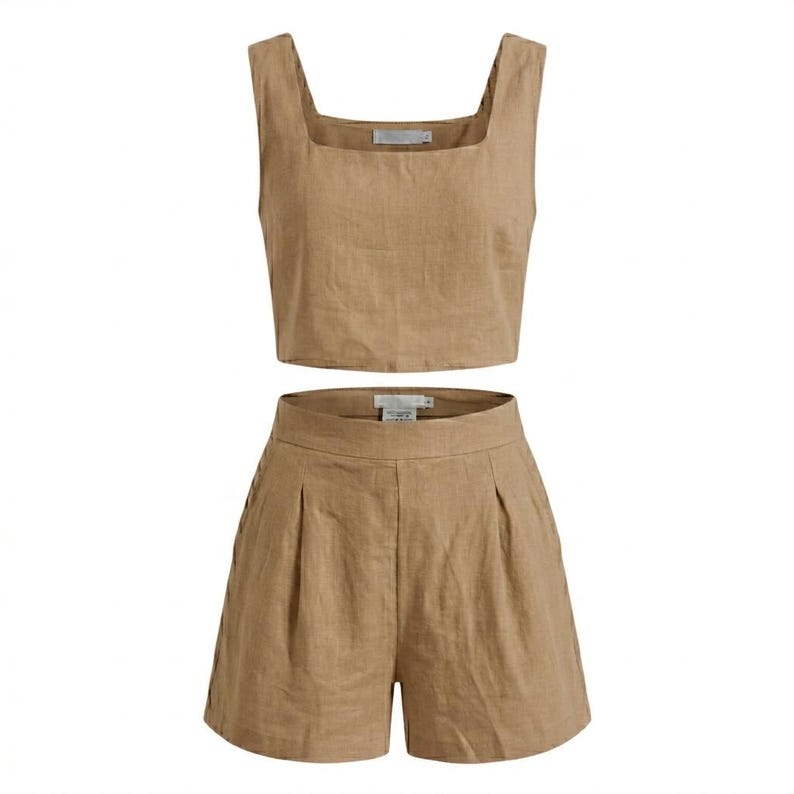 May include: A two-piece linen set in a neutral tan color. The set includes a square-neck crop top and high-waisted shorts with pleats. The fabric appears to be lightweight and suitable for warm weather.