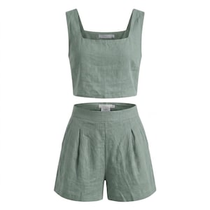 May include: Sage green two-piece outfit. The set includes a square-neck crop top and high-waisted shorts. The shorts have pleats in the front. The fabric appears to be linen or a similar lightweight material. The outfit is designed for warm weather.