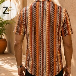 May include: Short-sleeved shirt with a vertical striped pattern in shades of orange, brown, and white. The shirt has a collared neckline and is made of a lightweight fabric. The back of the shirt is visible, showcasing the intricate design.